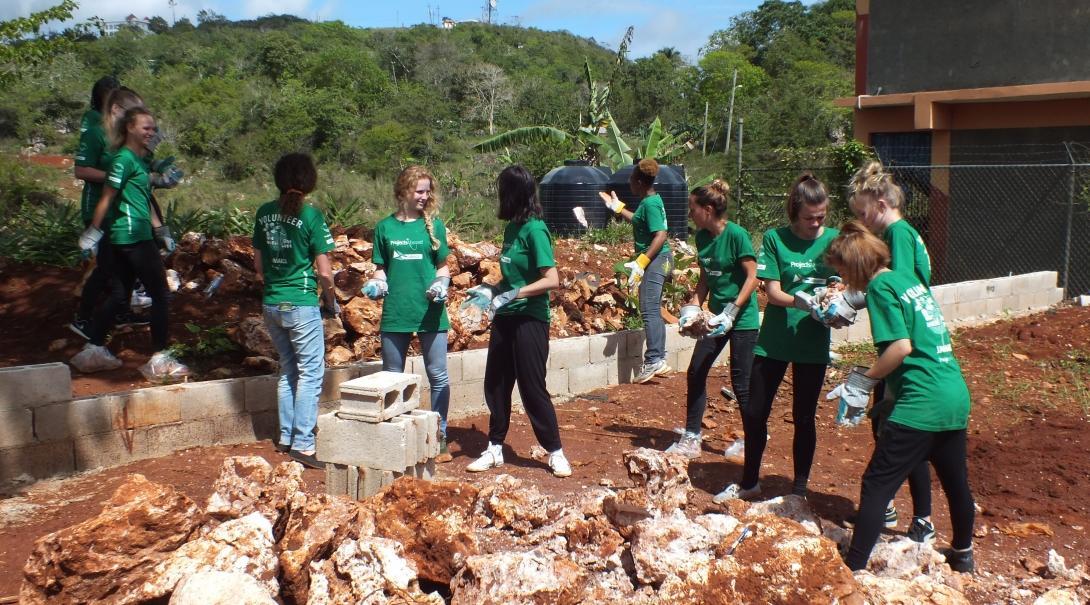 Volunteers team up to clear ground and build a playground at a disadvantaged school in Jamaica. A group doing building volunteer work in Jamaica help clear ground at a school to construct a playground.